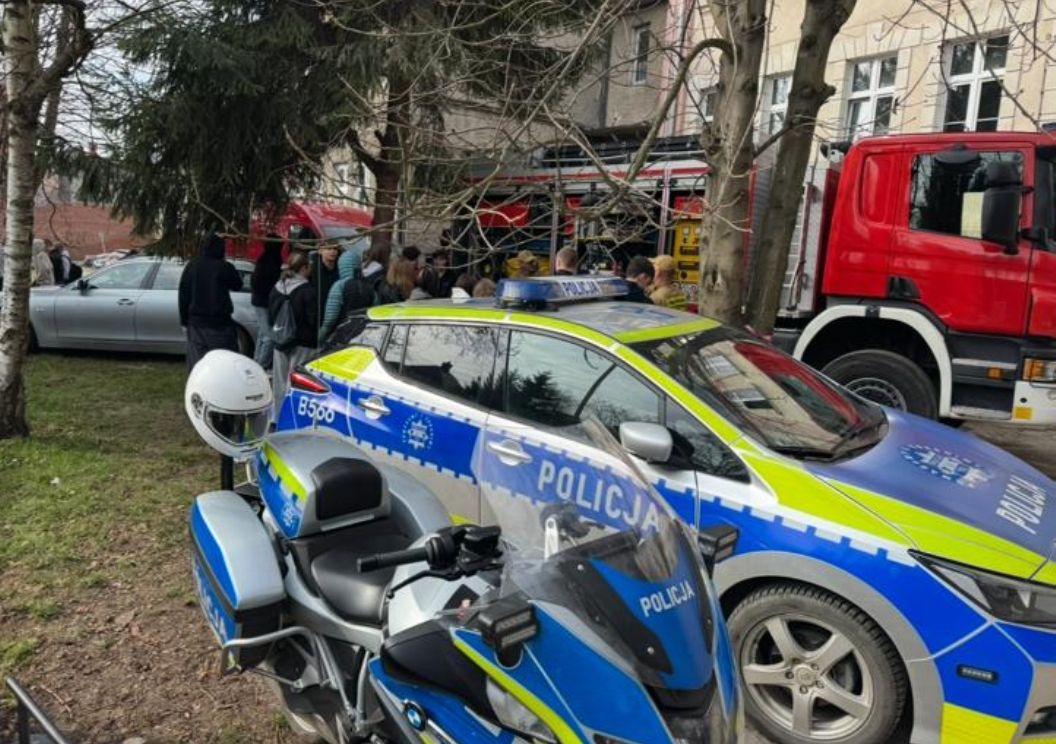 Policyjny radiowóz i motocykl zaparkowane na trawniku podczas Dni Otwartych szkoły, w tle wóz strażacki i zgromadzeni uczniowie