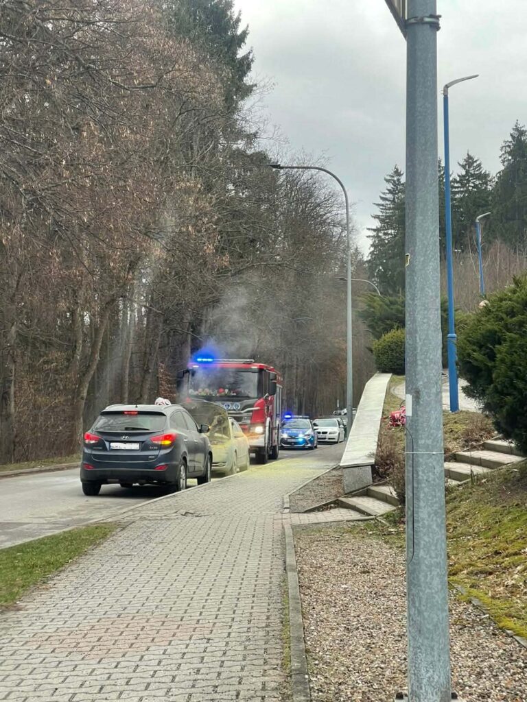 Wóz strażacki z włączonymi sygnałami świetlnymi podczas akcji gaśniczej pożaru samochodu na ulicy w Polanicy-Zdrój przy szpitalu