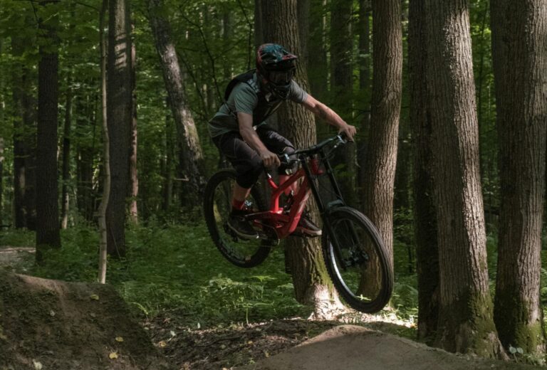 Zawodnik downhillu w pełnym ekwipunku wykonujący skok na rowerze górskim w lesie podczas zawodów w Kudowie-Zdroju
