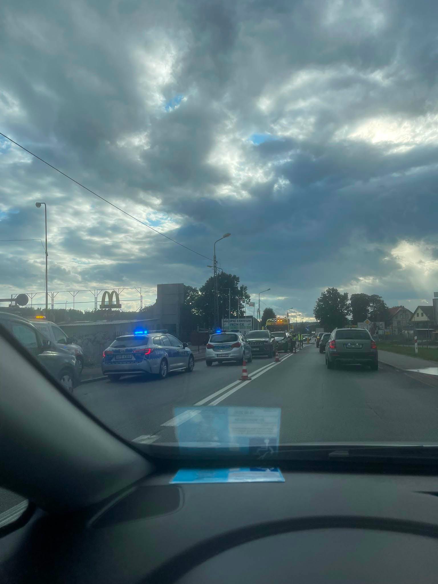 Radiowóz policyjny na sygnale i korek samochodowy w Kudowie-Zdroju obok restauracji McDonald's pod zachmurzonym niebem.